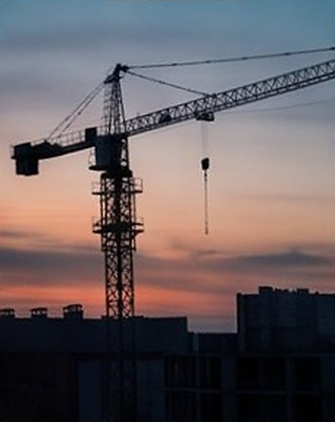 Силуэт башенного крана над строящимися домами на закате